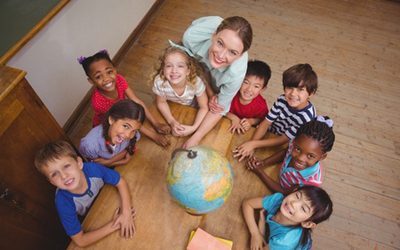 46212807 - cute pupils smiling around a globe in classroom with teacher at the elementary school